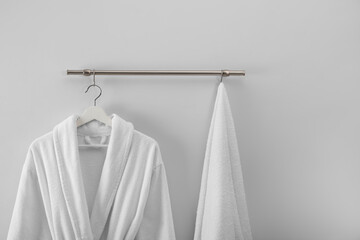 Hanger with clean bathrobe and towel on light wall