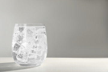 Glass of soda water with ice on white wooden table. Space for text