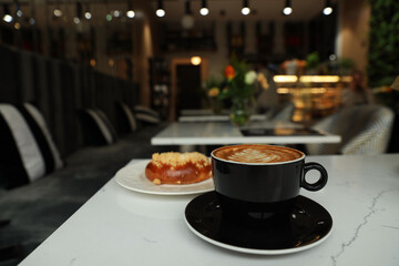 Cup of fresh coffee and bun on table in cafeteria