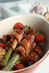 Oven baked asparagus wrapped with bacon in ceramic dish on white table, closeup