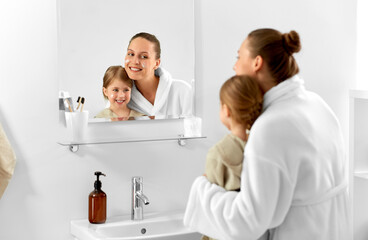 beauty, family and people concept - happy smiling mother and daughter with moisturizer on their faces looking to mirror in bathroom