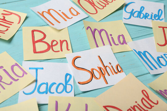 Paper notes with different baby names on light blue wooden table