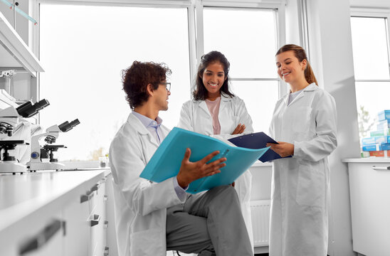 science research, work and people concept - international group of happy scientists with folder discussing report in laboratory