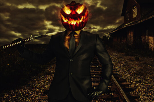Scary smiling jack-o-lantern character in suit with katana on shoulder. Abandoned train station in background.