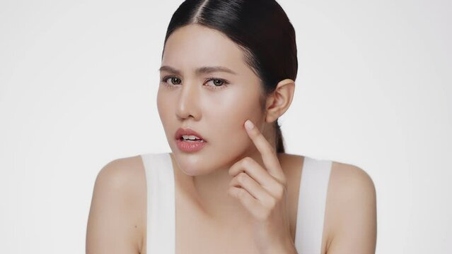 Unhappy young Asian woman squeezing her pimple, removing pimple from her face. Woman skin care concept.