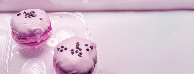 Two delicious donuts with icing sugar and chocolate chips in a transparent plastic container, a banner with a copy of the space on the right, pink tinting