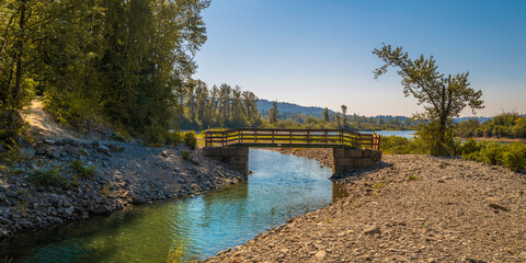 Old wooden footbridge connecting the rocky island to the hilly wooded mainland in Ruskin Park over the Stave River, British Columbia, Canada 