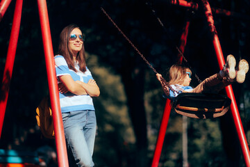 Cool Relaxed Mom Supervising Her Child at the Playground. Mother using sunglasses and UV protection for her and her child
