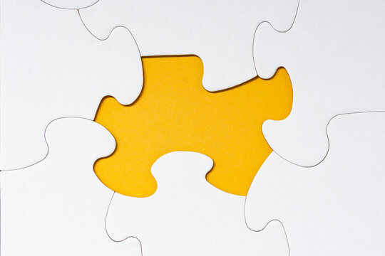 White jigsaw puzzle with some missing pieces on yellow background.