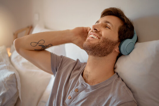 Man listening to music, podcast or radio with headphones at home while relaxing, smile and happy in his bedroom. Peaceful, freedom and young male streaming an online audio playlist enjoying weekend