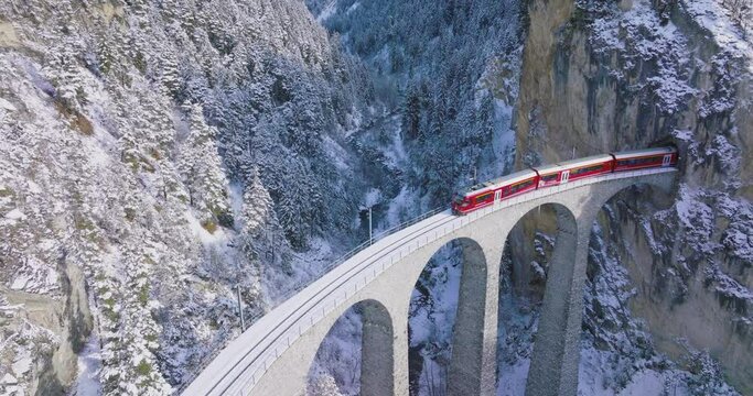 Landwasser Viaduct world heritage sight with luxury Glacier and Bernina express in Swiss Alps snow winter scenery. Aerial Drone shot red train passing through famous mountain in Filisur, Switzerland.