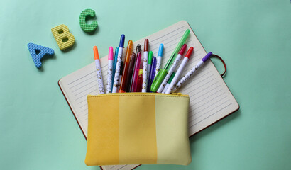 Bolsa amarilla con plumones de colores sobre cuaderno de rayas y letras de goma del abecedario en...