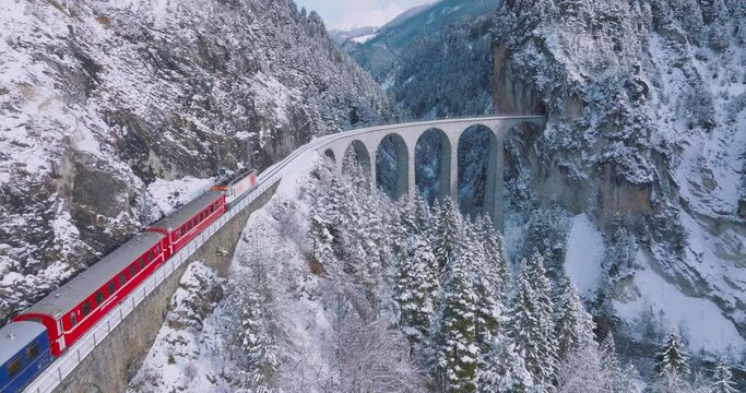 Landwasser Viaduct world heritage sight with luxury Glacier and Bernina express in Swiss Alps snow winter scenery. Aerial Drone shot red train passing through famous mountain in Filisur, Switzerland.