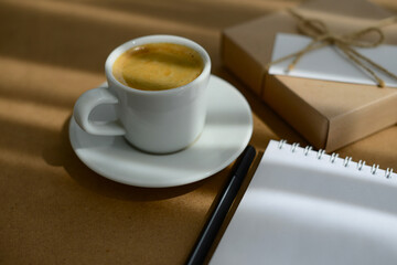 A cup of coffee on desktop. Coffee break. Coffee, notepad, workplace and gift box with blank greeting card, soft focus, blurred background