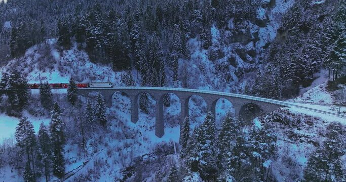 Landwasser Viaduct world heritage sightseeing Glacier and Bernina express in Swiss Alps snow winter scenery at night. Aerial Drone shot red train passing through famous mountain. Filisur, Switzerland.