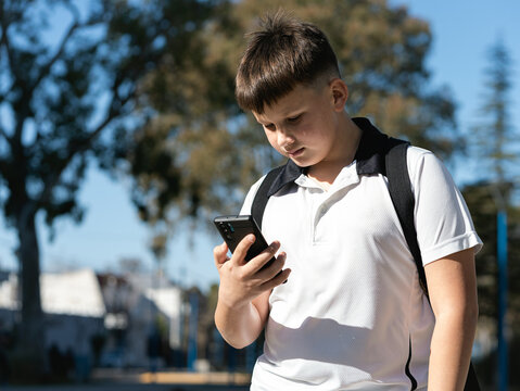 Schoolboy looking at the phone outdoors - Powered by Adobe