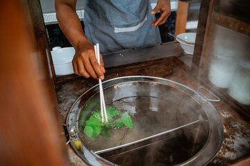 close up of man's hand boiled vegetables when prepare chicken noodle dish on the cart