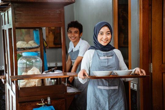 female muslim seller in apron bringing chicken noodle dish with bowl on tray for customer