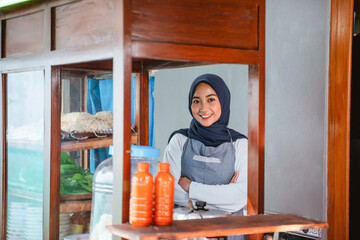 female seller in hijab wearing apron standing with crossed hands behind cart