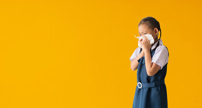 Asian student little girl sick with sneezing on the nose and cold cough on tissue paper because weak or virus, isolated on yellow background with Clipping paths for design work empty free space - Powered by Adobe