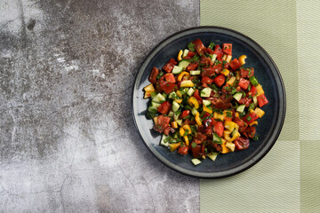 Summer homemade tomato, cucumbers and bell pepper salad in a bowl on a dark background. Top view, flat lay .