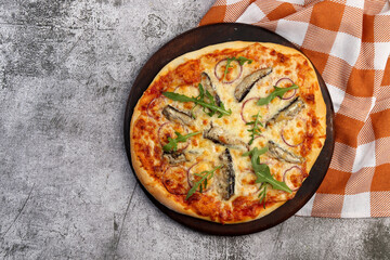 Homemade Sardine Pizza on a round wooden cutting board on a dark grey background. Top view, flat lay