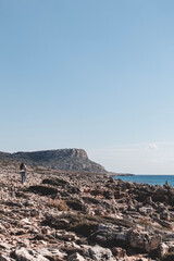 Young woman from behind is walking in a desert ground to the mountain Cape Greco