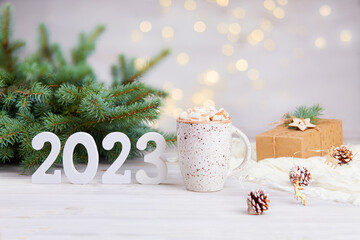 Happy New Year greeting card 2023. A mug of cocoa with marshmallows, a gift in kraft paper, white...