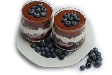 Traditional Italian dessert called Tiramisu with mousse and chocolate cookies and fresh blueberries in glass. Homemade layered cakes on white background 
