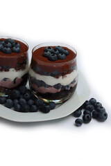 Traditional Italian dessert called Tiramisu with mousse and chocolate cookies and fresh blueberries in glass. Homemade layered cakes on white background 