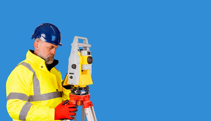Fototapeta premium A builder in a blue helmet, yellow reflective hi-visibility coat and red safety gloves on white background with space for text using modern surveying equipment. 