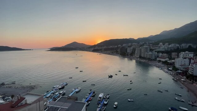 lovely sunset over rafailovici in montenegro, high flying drone shot in the evening on a sunny day during sunset, sun setting over the mountain with boats and cars in the view.