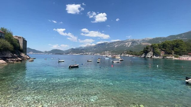 Blue water and boats surrounding Sveti Stefan in montenegro with tall mountains in the background, very famous beach where all of the current celebrities go when they want to have a lovely holiday