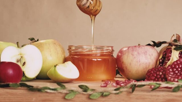 Golden liquid honey pouring on fresh apples. Happy Rosh Hashanah concept. Wooden spoon for honey in human hand. Traditional food of jewish new year celebration.
