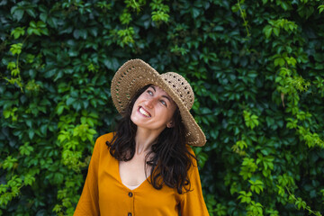 A smiling girl in a straw hat stands near a wall overgrown with ivy