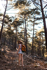 A woman with a backpack and a straw hat on a mountain path