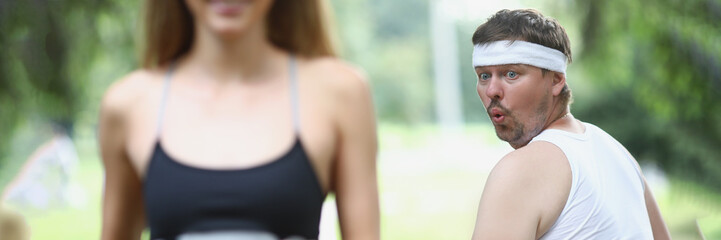 Fat man looking at young woman athlete jogging in park