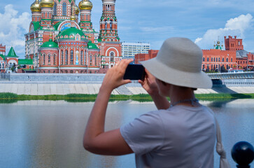 Fototapeta premium Woman tourist in a straw hat makes a mobile photo on a city street