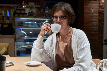 A girl in casual clothes sits in a cafe with a cup of coffee in her hands