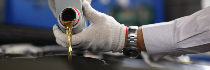 Master repairman pouring engine oil under hood of car closeup