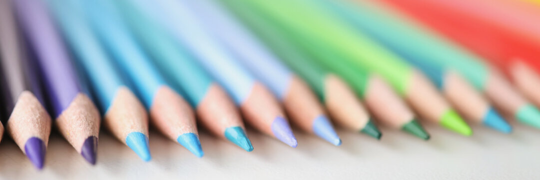 Many sharp multicolored pencils lying over colors of rainbow closeup background