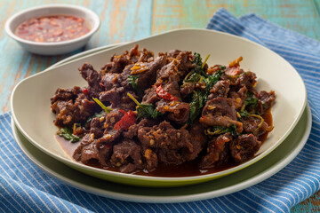Beef pad kra pao or spicy stir-fried holy basil beef slices, served on a white-beige plate together with garlic chili relish. Pad krapao is one of popular Thai food dishes. - obrazy, fototapety, plakaty