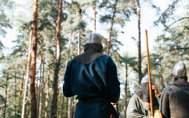 Back view of a warrior wearing ancient clothes and a helmet with a spear standing in the forest...
