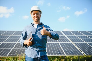 The portrait of a young engineer checks with tablet operation with sun, cleanliness on field of photovoltaic solar panels. Concept: renewable energy, technology, electricity, service, green power