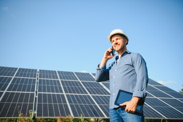 Male engineer in a helmet standing near the solar panels, looking up. Green ecological power energy...