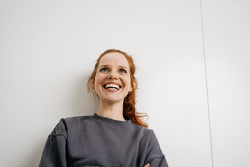 young redhead woman in front of white wall looking up laughing