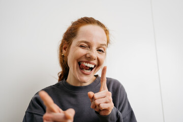 young redhead woman in front of a white wall and makes faces