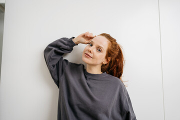 young redhead woman in front of a white wall and looks thoughtfully into the camera