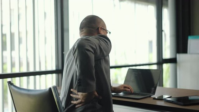 Man texting on keyboard laptop work so hard and long time that he has office syndrome. Salaryman working his computer suddenly feeling pain in back and waist He try to relax and relieve by his hand.