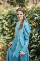 Young beautiful girl dressed in a blue vintage dress   with a bow on her head. Victorian girl in a...